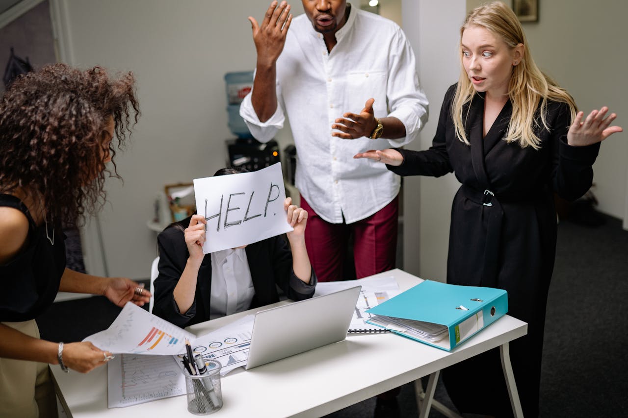 A group of employees in heated discussion, one holding a HELP sign, indicates workplace stress.